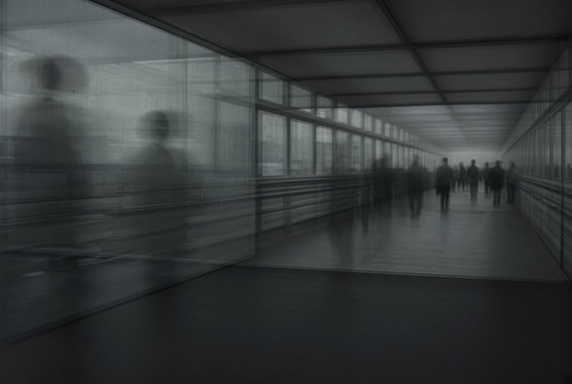 Blurred silhouettes of people walking through a modern glass corridor with polished floor and overhead lighting
